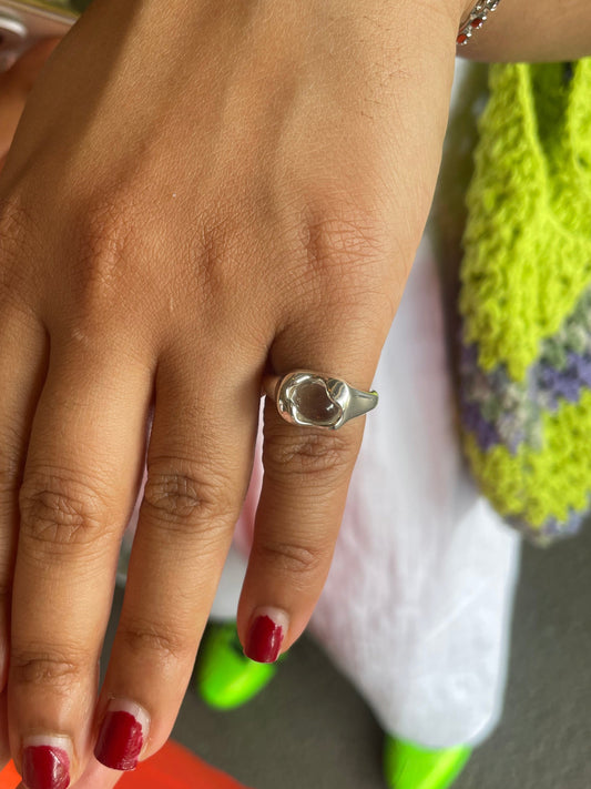 Hand with red nail polish wearing a silver ring, blurred background